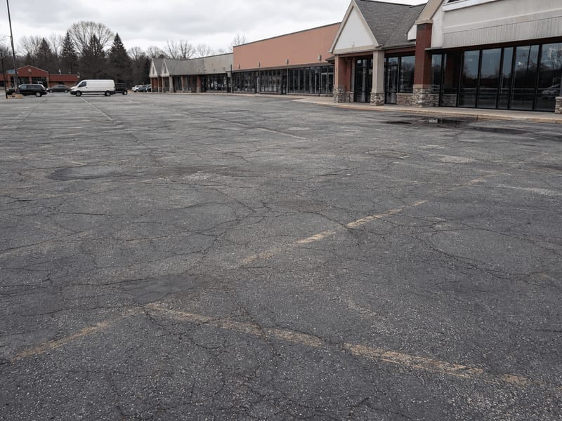 De Pere retail center parking lot before restoration, showing cracking and faded striping